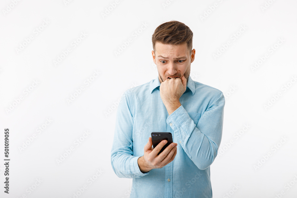 Portrait of a man in a desperate situation. The man looks at the smartphone, extremely confused and alarmed because of the failure. Portrait of a man in a desperate situation. The man looks at the smartphone, extremely confused and alarmed because of the failure.