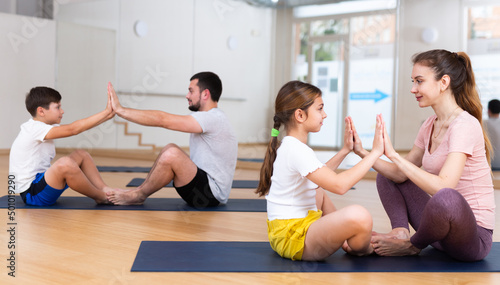 Young woman practicing yoga in pair with her teen daughter during family workout at gym