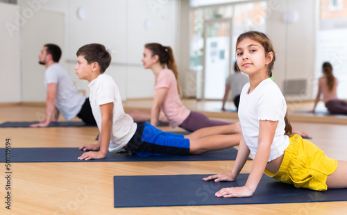 Sporty teen girl practicing yoga positions during family workout at fitness center, performing stretching asana Urdhva Mukha Shvanasana known as Upward Facing Dog