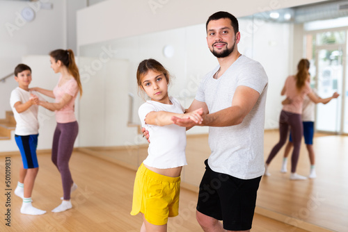 Young adult man practicing dance in pair with his tween daughter during family dance class