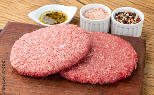 Raw meat hamburger over wooden board with seasonings