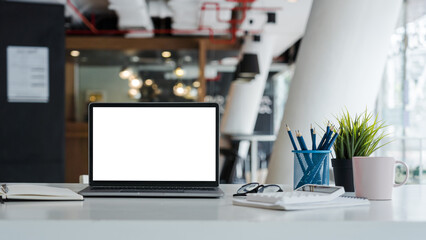 Mockup laptop computer with white screen put on desk table of business office.