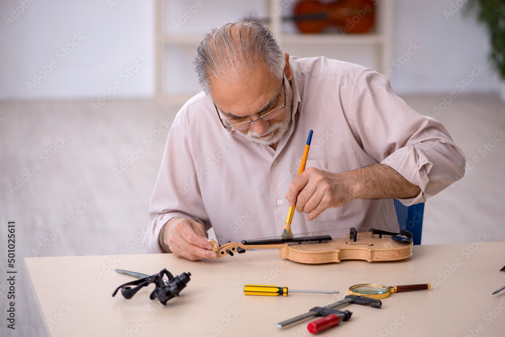 Old male repairman repairing musical instruments at workshop Old male repairman repairing musical instruments at workshop