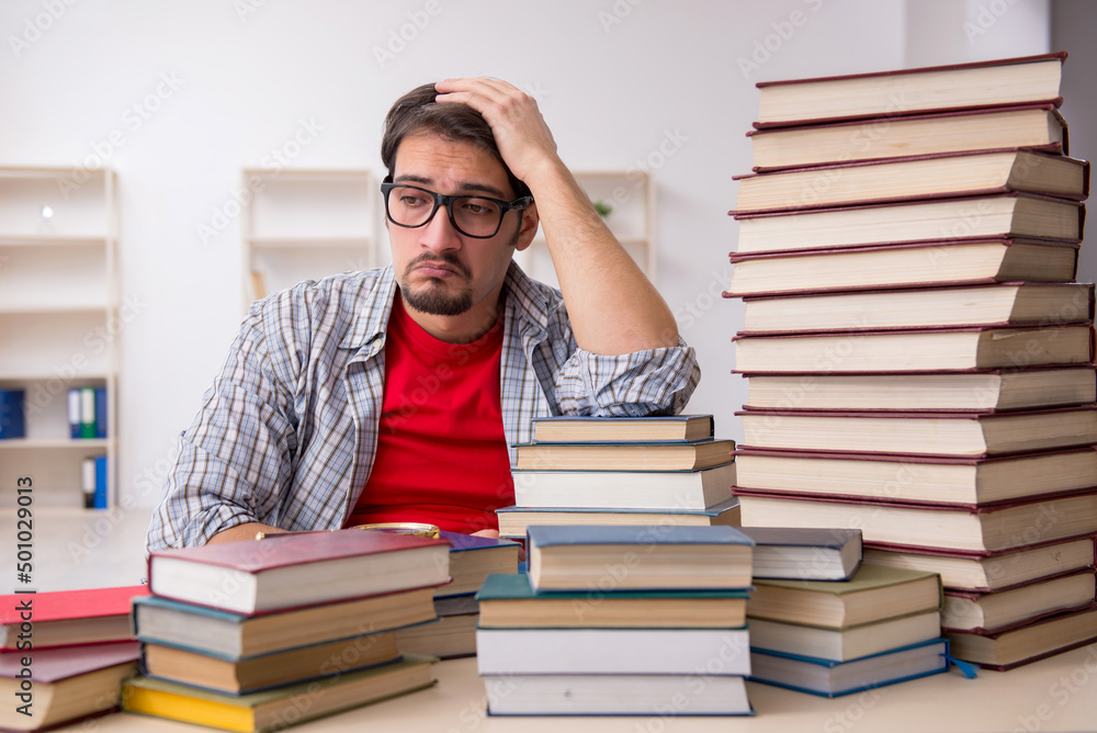 Young male student and too many books in the classroom Young male student and too many books in the classroom
