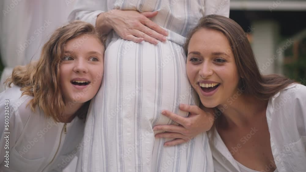 Pregnant belly of unrecognizable woman with excited young lady and teenage girl listening smiling. Positive Caucasian sisters rejoicing friend pregnancy. Slow motion Pregnant belly of unrecognizable woman with excited young lady and teenage girl listening smiling. Positive Caucasian sisters rejoicing friend pregnancy. Slow motion