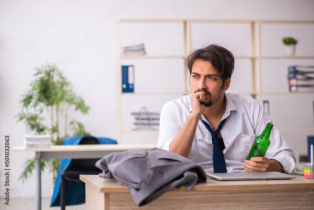 Young alcohol addicted employee sitting in the office Young alcohol addicted employee sitting in the office