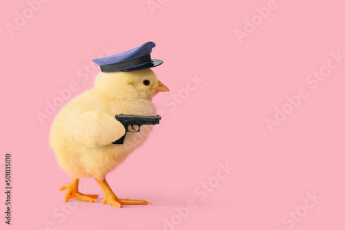 Funny little chick in policeman's hat and with gun on pink background