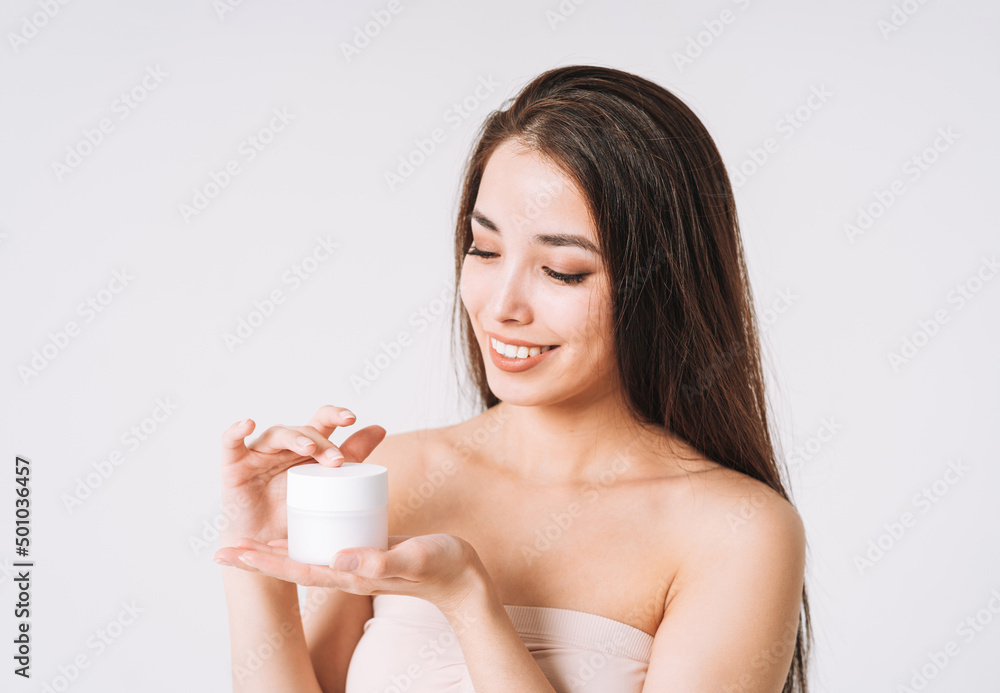 Beauty portrait of happy smiling asian woman with dark long hair put day nourishing moisturizer cream on clean fresh skin face and hands on white background Beauty portrait of happy smiling asian woman with dark long hair put day nourishing moisturizer cream on clean fresh skin face and hands on white background