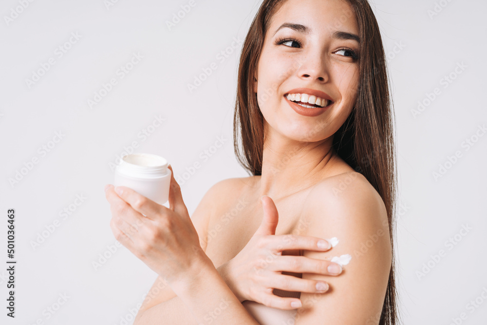 Beauty portrait of happy smiling asian woman with dark long hair put day nourishing moisturizer cream on clean fresh skin face and hands on white background
