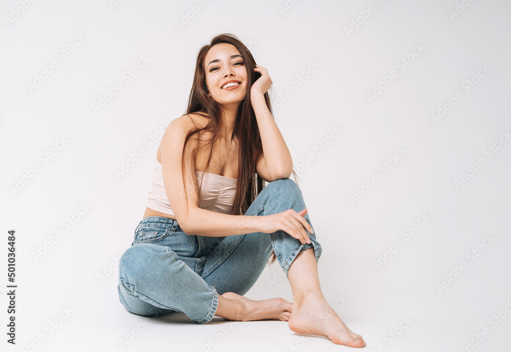 Portrait of happy young beautiful asian woman with dark long hair in jeans sitting on white background isolated Portrait of happy young beautiful asian woman with dark long hair in jeans sitting on white background isolated