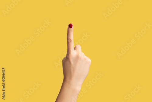 Profile side view closeup of woman hand with red manicure showing number one with finger or showing up side. Indoor studio shot isolated on yellow background. photo