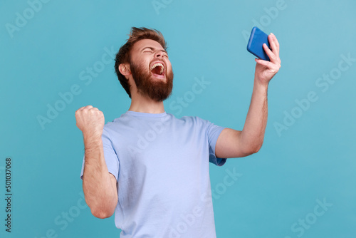 Foto Portrait of extremely happy handsome bearded man gamer playing video game on mobile phone, celebrating victory, complete level