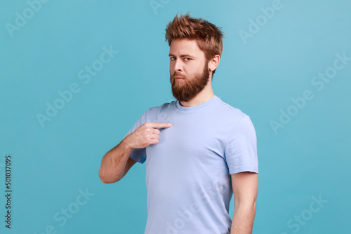 This is me. Portrait of self-confident narcissistic bearded man standing pointing himself, feeling self-important, proud, famous. Indoor studio shot isolated on blue background. photo