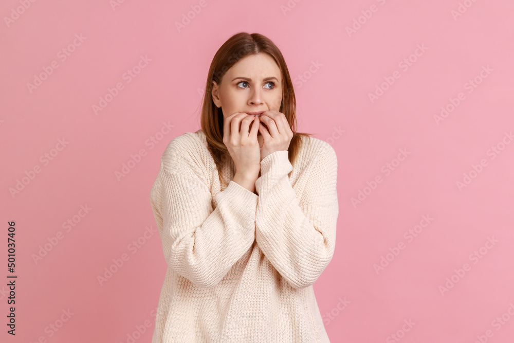Portrait of nervous young adult blond woman thinking and worried about work, deadlines and biting her nails, wearing white sweater. Indoor studio shot isolated on pink background. Portrait of nervous young adult blond woman thinking and worried about work, deadlines and biting her nails, wearing white sweater. Indoor studio shot isolated on pink background.