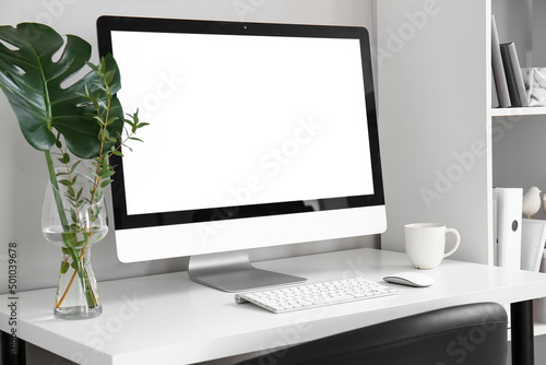 Workplace with computer, plant branches in vase and cup near light wall