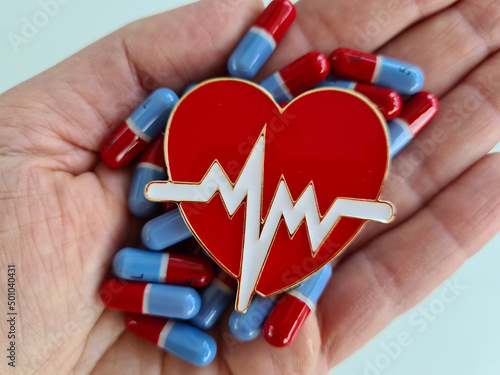 Person holds heart pills and cardiological heart in hand