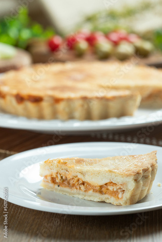 Close up piece of Chicken pie with cottage cheese, tomatoes, onion and olives on wooden table and white plate.