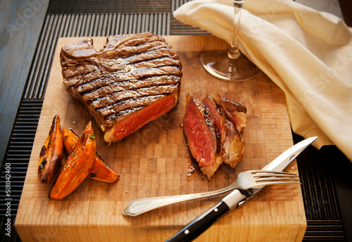 Partially Sliced Steak on a Cutting Board with Sweet Potato Fries; Wine Glass photo