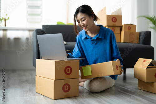 Shipping shopping online, startup small business owner writing address on cardboard box at workplace. Freelance Asian woman small business entrepreneur SME working with box at home