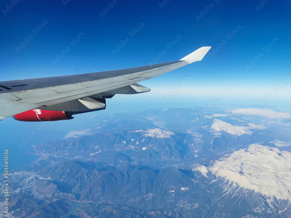 View from the porthole on the wing of an airplane with a red aircraft engine flying to Cyprus in the morning over beautiful mountains with snowy peaks. View from the porthole on the wing of an airplane with a red aircraft engine flying to Cyprus in the morning over beautiful mountains with snowy peaks.