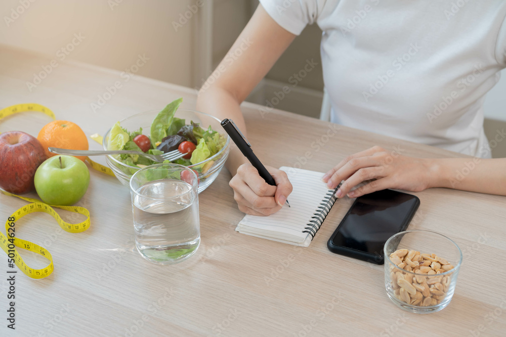 Diet, Dieting hand of asian young woman working, write diet plan right nutrition with eat fresh vegetables salad is food for good health not eat junk food. Nutritionist female, Weight loss of healthy. Diet, Dieting hand of asian young woman working, write diet plan right nutrition with eat fresh vegetables salad is food for good health not eat junk food. Nutritionist female, Weight loss of healthy.