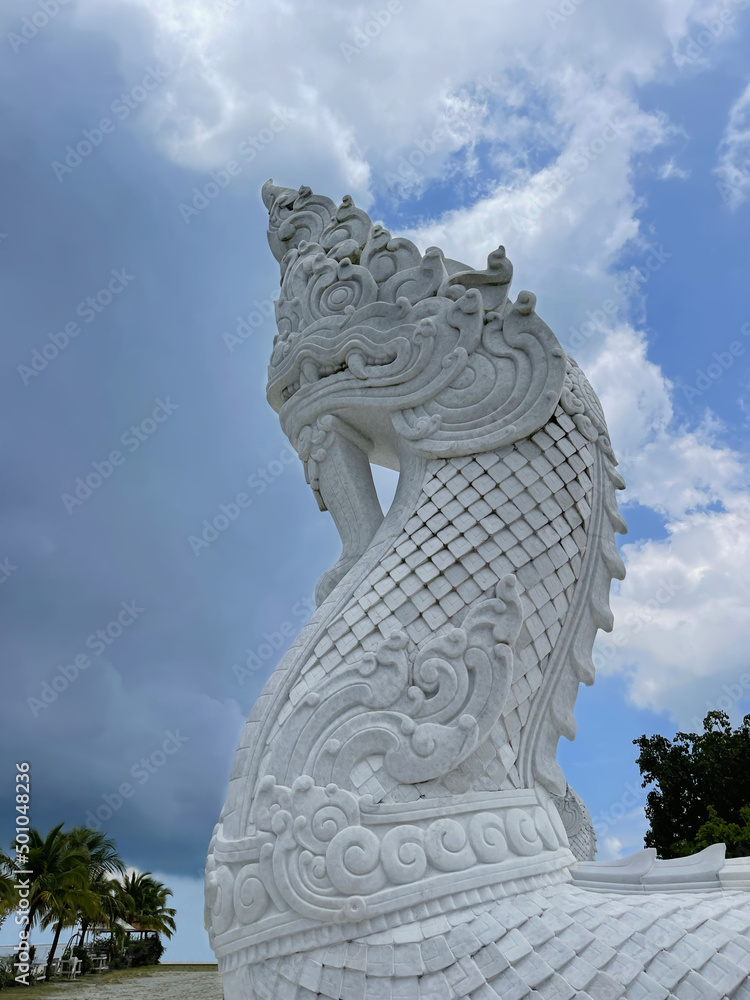 Marble statue of a serpen's head reaching towards the sky. Monument in white marble. Asian snake symbol. Blue skies clouds backdrop. View from bottom to top. Macro, close-up, isolated. Thailand, China