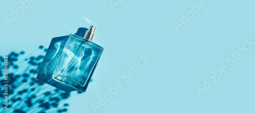 Transparent bottle of perfume on a blue background. Fragrance presentation with daylight. Trending concept in natural materials with plant shadow. Women's and men's essence.