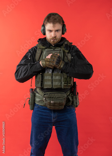 airsoft player in full gear with guns GG RK74. a man in headphones, body armor, with a backpack and a belt. isolated, red background.