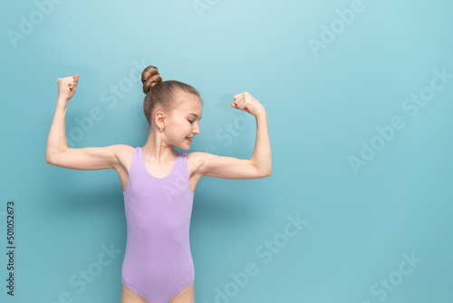 A young gymnast girl, stretching her muscles, imagine that she has a powerful arm with big biceps