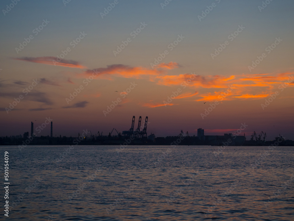 Beautiful sunset above port with silhouettes of cargo cranes. Industrial black sea port Odesa, Ukraine with a lot of cranes, cabins, boxes and tanks by the water at evening dusk