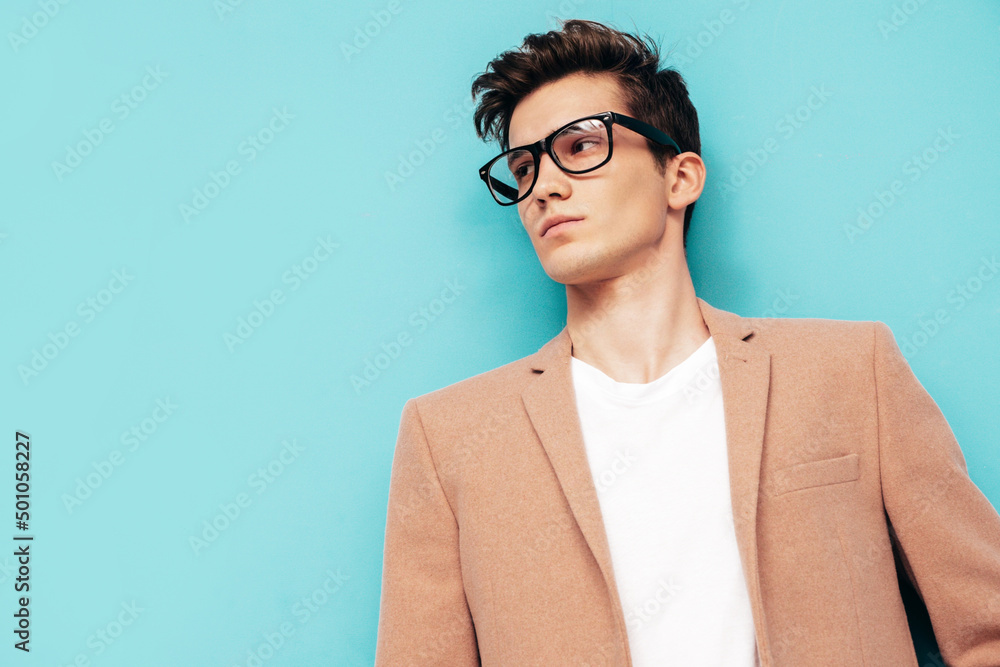 Closeup portrait of handsome confident stylish hipster lambersexual model. Sexy modern man dressed in elegant beige suit. Fashion male posing in studio near blue wall. In spectacles Closeup portrait of handsome confident stylish hipster lambersexual model. Sexy modern man dressed in elegant beige suit. Fashion male posing in studio near blue wall. In spectacles