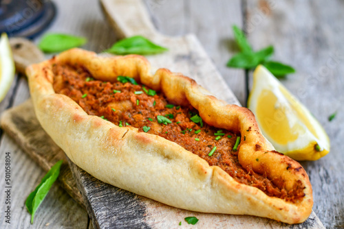  Traditional Turkish cuisine. Baked Pide dish with minced  beef, tomatoes and  herbs on  wooden background.  Turkish pizza pide