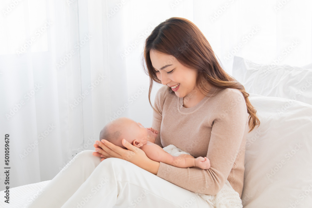 Selective focus Beautiful Asian mother supports and tenderly cuddles newborn baby gently while infant lying on lap. Mom looking and lift baby with love and care. Toddler deeply sleeping on woman lap. Selective focus Beautiful Asian mother supports and tenderly cuddles newborn baby gently while infant lying on lap. Mom looking and lift baby with love and care. Toddler deeply sleeping on woman lap.