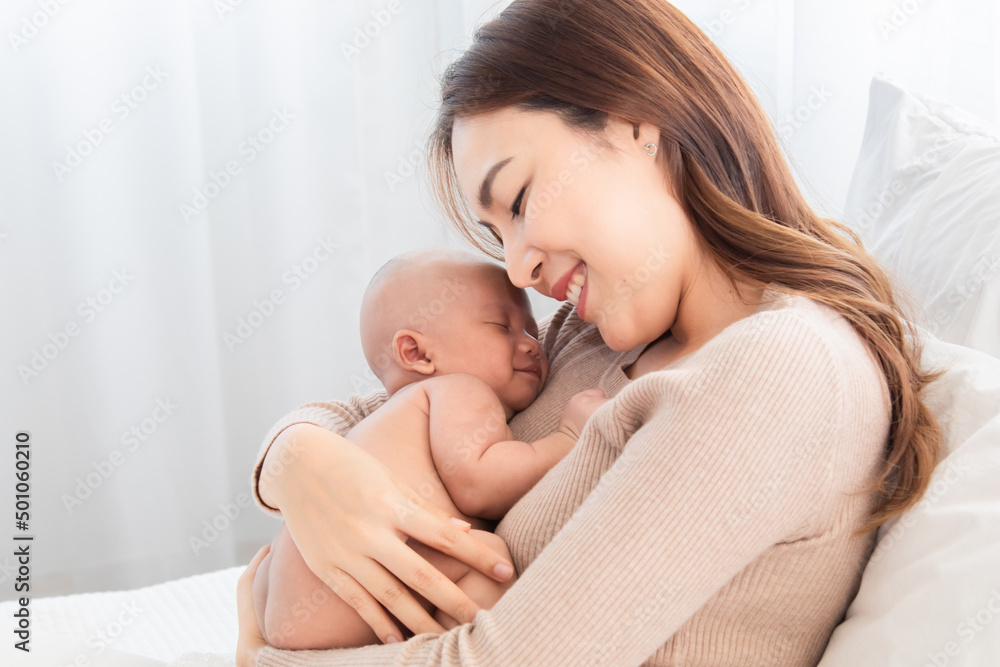 Beautiful Asian mother supports and tenderly cuddles newborn baby while toddler is sleeping on mom chest, Mother looking adorable infant with love and care. woman and child lying on bed together. Beautiful Asian mother supports and tenderly cuddles newborn baby while toddler is sleeping on mom chest, Mother looking adorable infant with love and care. woman and child lying on bed together.