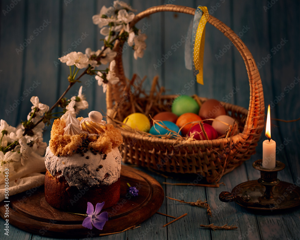 Easter compositio. Easter cake, a basket with colored eggs, a bronze candlestick with burning candles and spring flowers with a blurry background.
