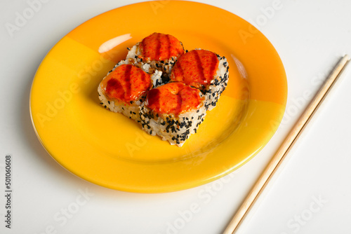 Traditional Japanese food, Asian cuisine. Close-up yellow plate with hot baked rolls and chopsticks on white table