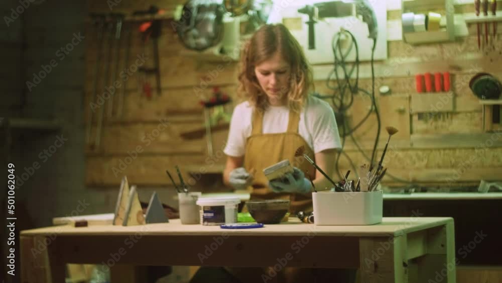 A woman paints a wooden part of a wooden product with a brush. Business idea for a home workshop A woman paints a wooden part of a wooden product with a brush. Business idea for a home workshop