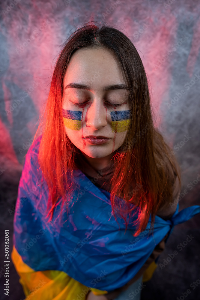 Pretty frightened woman with Ukraine flag on face isolated on dard background