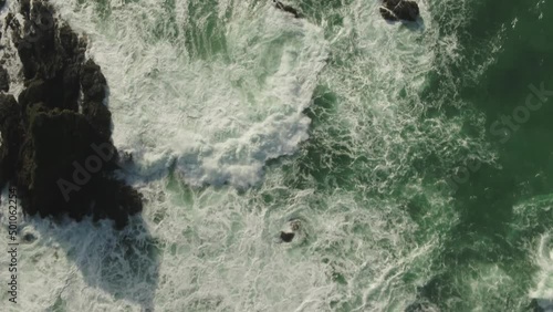 Aerial looking down at waves crashing over rocks towards shore.