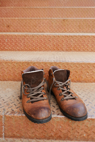 Fotografija Old worn brown leather shoes with laces on a metal ladder