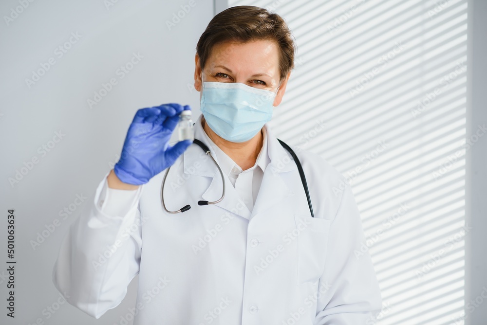 Closeup hand of woman doctor or scientist in doctor's uniform wearing face mask protective in lab holding medicine liquid vaccines vial bottle, coronavirus or COVID-19 concept.