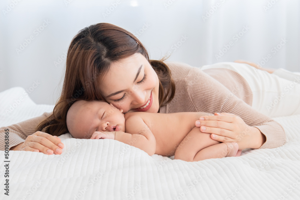 Beautiful asian mom supports and tenderly cuddles newborn baby gently while baby sleeping. Young woman kissing and touching on back child with love and tender. Mother and infant spend time together. Beautiful asian mom supports and tenderly cuddles newborn baby gently while baby sleeping. Young woman kissing and touching on back child with love and tender. Mother and infant spend time together.