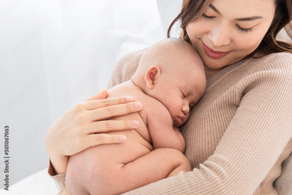 Beautiful Asian mother supports and tenderly cuddles newborn baby while toddler is sleeping on mom chest, Mother looking adorable infant with love and care. woman and child lying on bed together. Beautiful Asian mother supports and tenderly cuddles newborn baby while toddler is sleeping on mom chest, Mother looking adorable infant with love and care. woman and child lying on bed together.