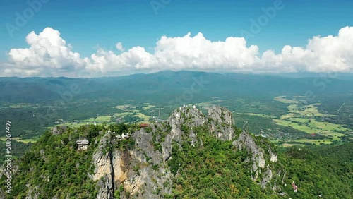 Drone moving towards the nearest mountain where there is a temple with pagodas on each top, all surrounded by dense vegetation in northern thailand photo