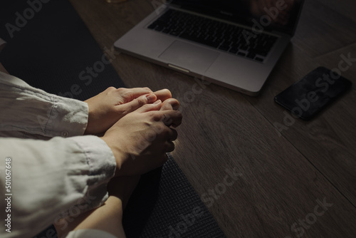 From above of crop woman touching bare feet and sitting on yoga mat with laptop during meditation at home lit by sunlight  © Dzmitry