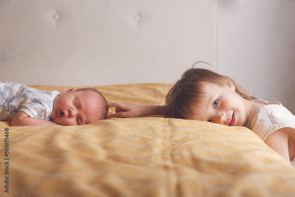 Cute bald chubby baby 2 months old and sister on bed in bedroom, baby