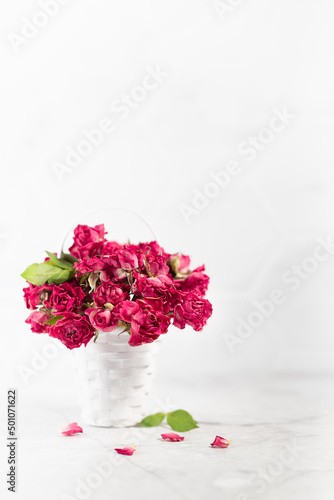 Fototapeta Naklejka Na Ścianę i Meble -  Romance dry pink roses in white basket as bridal bouquet on soft light white table and elegant marble wall, copy space, vertical. Elegant floral background for wedding, anniversary, greeting card.
