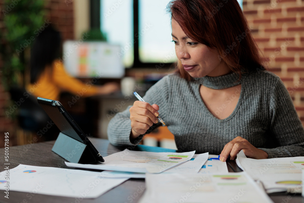 Portrait of asian businesswoman analyzing management graphs on tablet computer working at business strategy in startup office. Executive manager standing at table planning partnership Portrait of asian businesswoman analyzing management graphs on tablet computer working at business strategy in startup office. Executive manager standing at table planning partnership