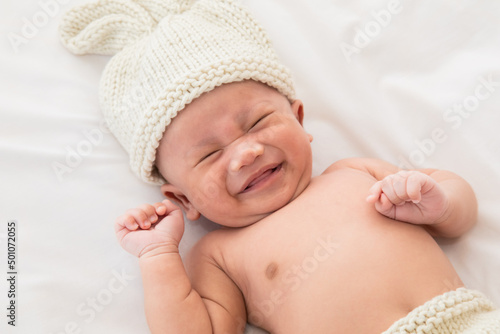 Adorable infant 0-1month fussy screaming unhappy angry. Child wearing pants and rabbit hat beige knitted tired and hungry.