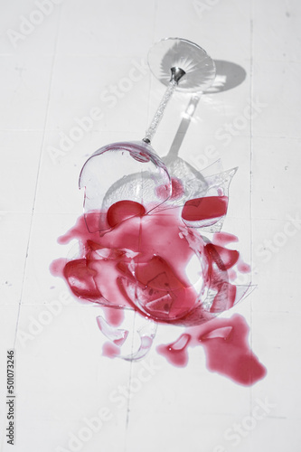 Broken glass with red wine on a table with white tiles